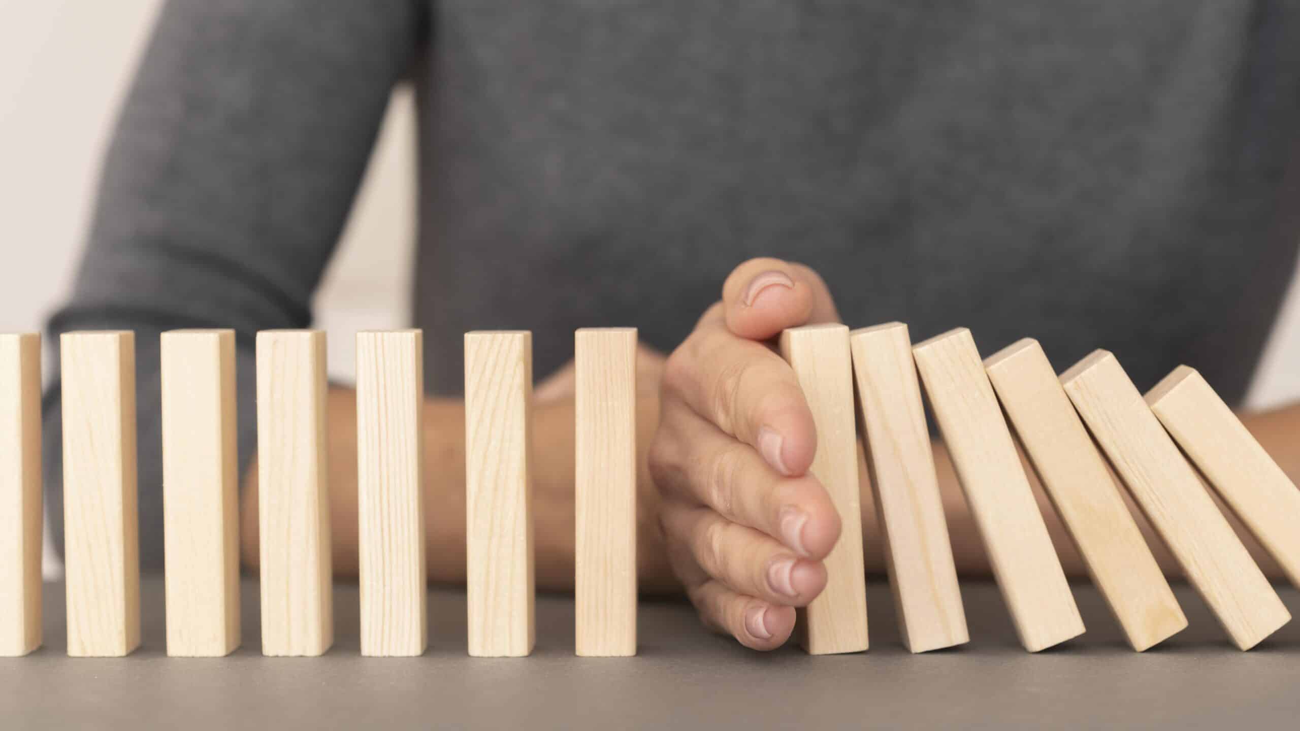 Dominosteine kippen um bis eine Hand den Fall stoppt